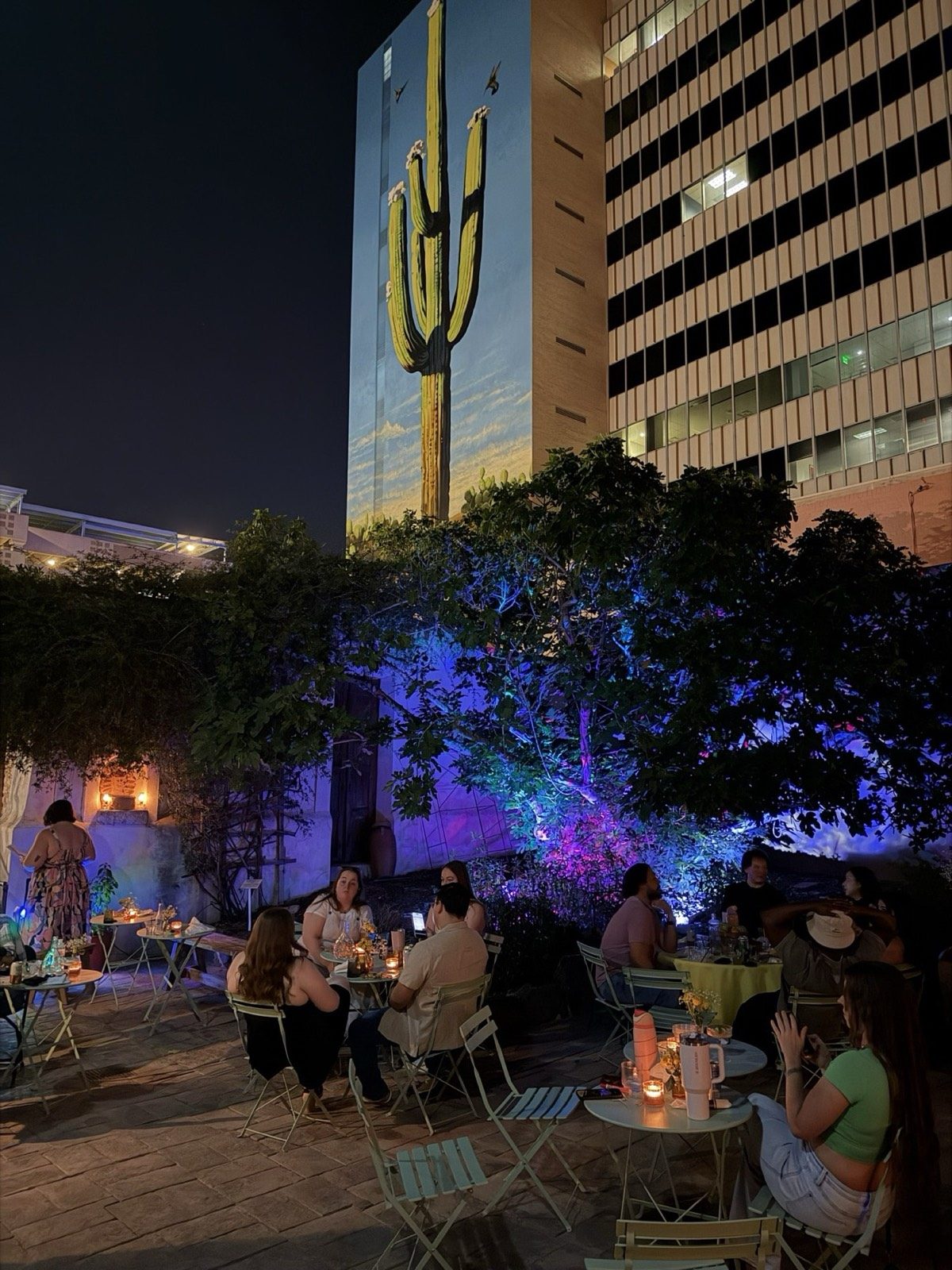 The candlelit Presidio courtyard at night, string lights above the tables and the saguaro mural behind