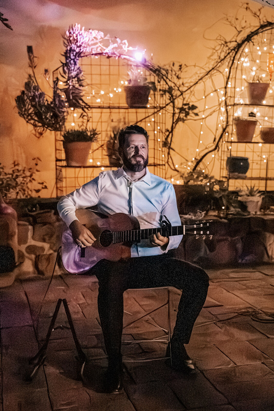 A guitarist playing among candles and potted plants