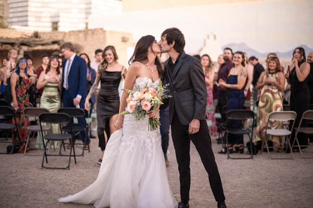 The newlyweds kissing on the aisle as guests cheer
