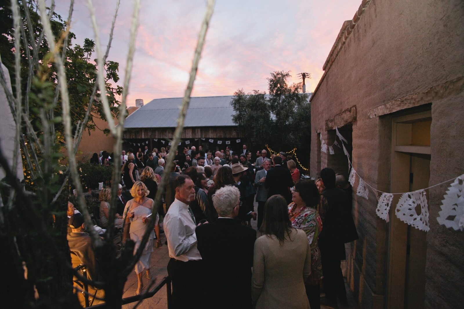 Wedding guests gathered in the courtyard at dusk under papel picado