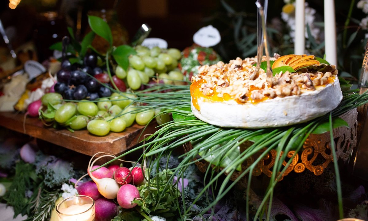 A candlelit grazing table with a nut-topped brie wheel, grapes and radishes